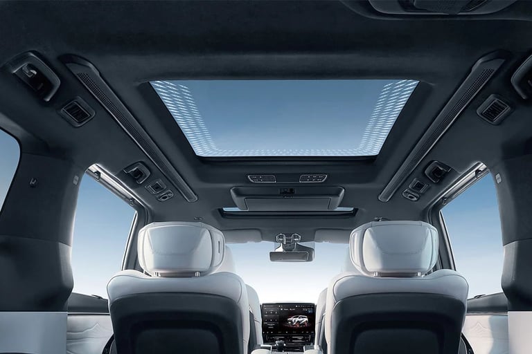 Interior view of a car with panoramic sunroof, white headrests, dark dashboard, and windshield showing clear sky